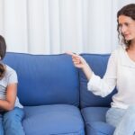 A woman and a young girl sit together on a couch, smiling and enjoying each other's company.