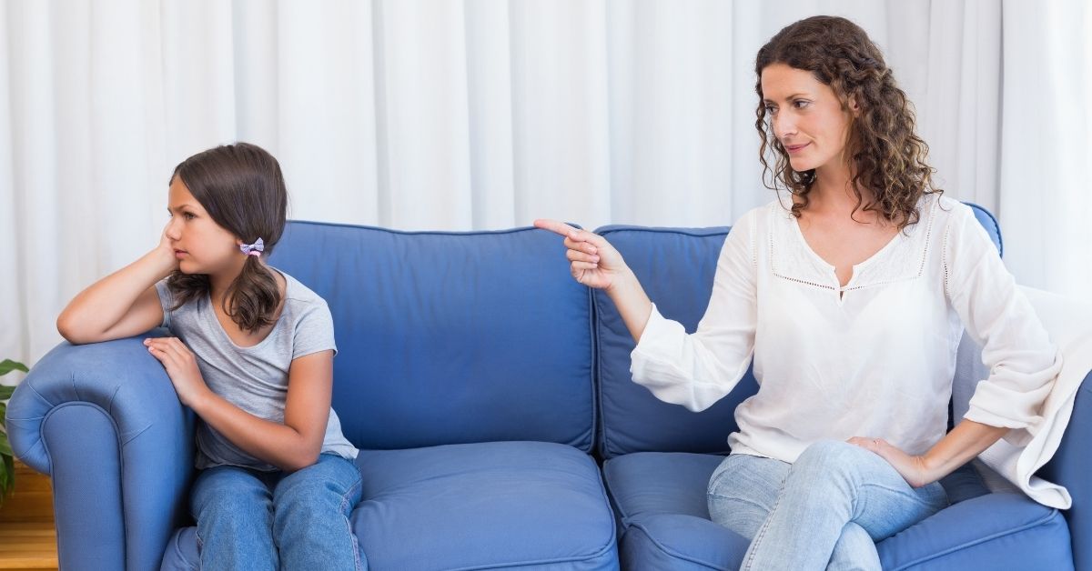 A woman and a young girl sit together on a couch, smiling and enjoying each other's company.