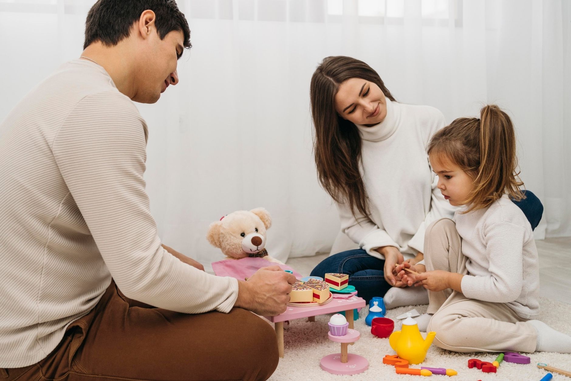 A family of four playing with colorful toys on a carpeted floor, smiling and enjoying their time together.
